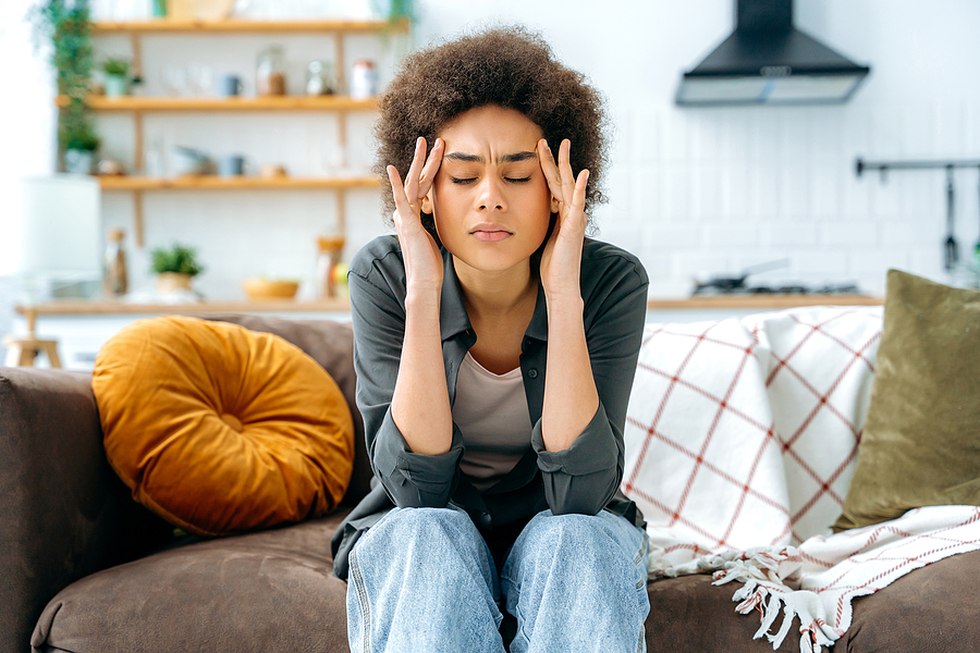 woman sitting on couch, eyes closed, rubbing her temples