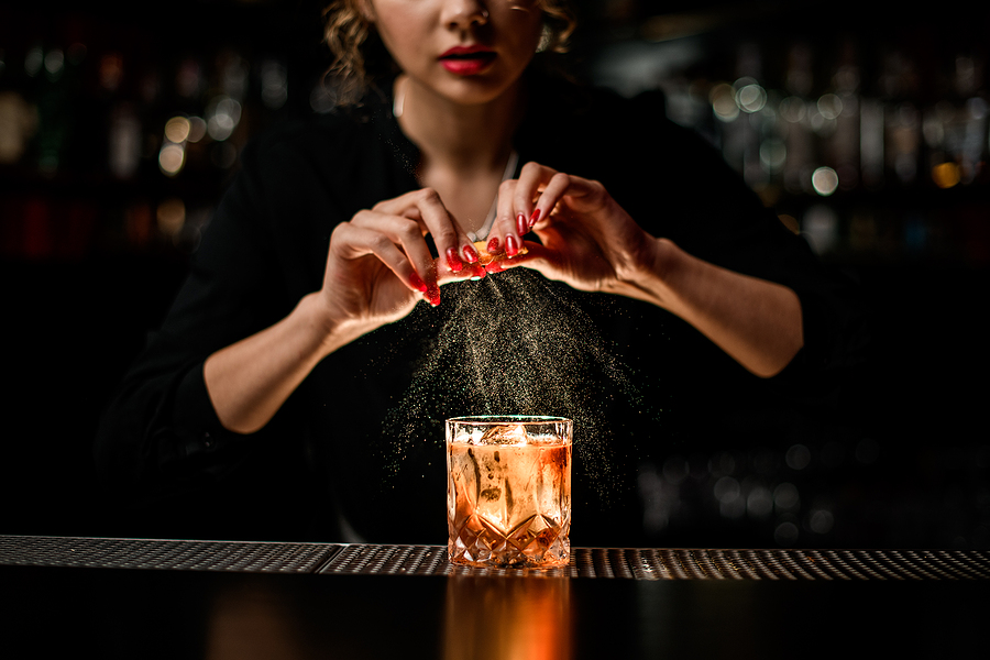 Bartender twisting lemon peel over cocktail glass on bar